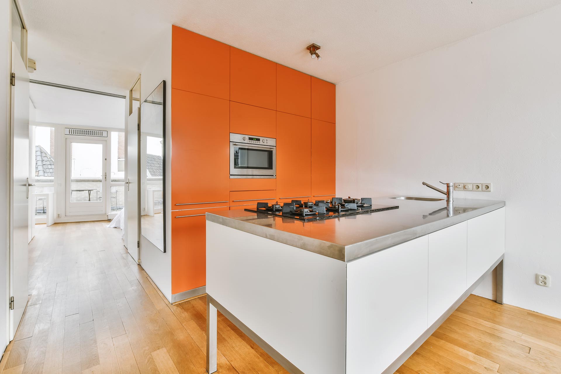 An orange kitchen featuring white cabinets and a stainless steel sink, creating a vibrant and modern cooking space.