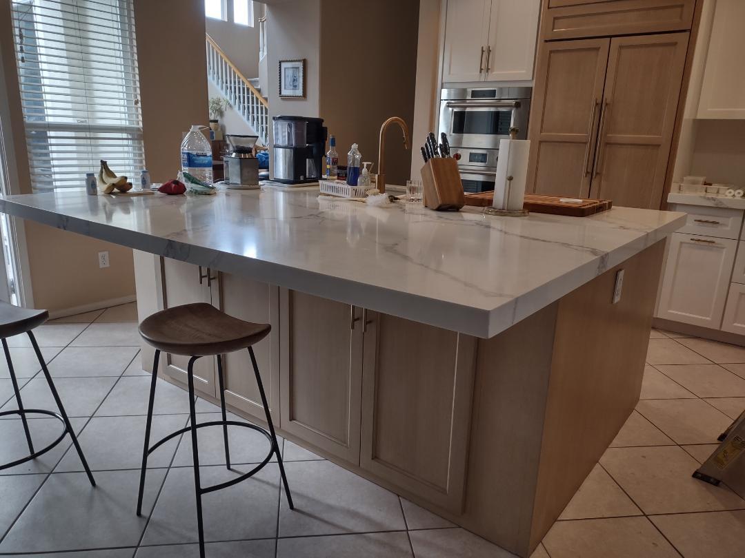 A modern kitchen featuring a large island with two stools positioned at one side.