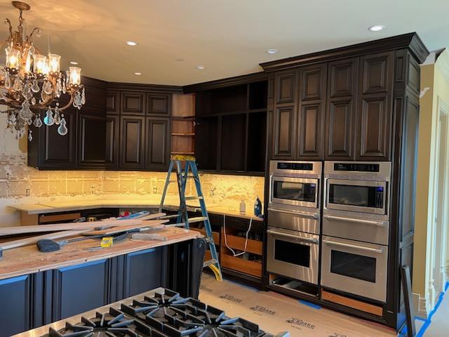 A modern kitchen featuring dark cabinets and an elegant chandelier hanging from the ceiling.